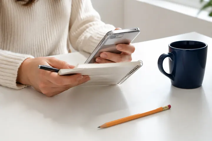 Persona comparando opciones en su celular y una libreta